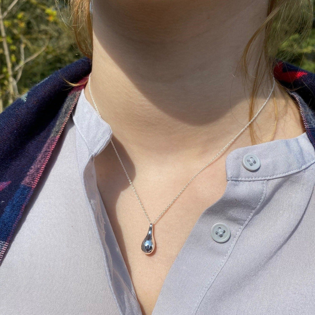 A Sterling Silver hammered teardrop pendant, hung on a silver chain and worn on a models neck.