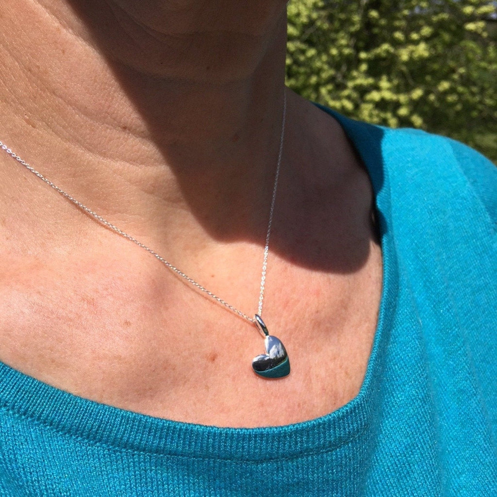 Sterling Silver solid heart pendant, hanging on a silver chain and worn on a ladies neck.