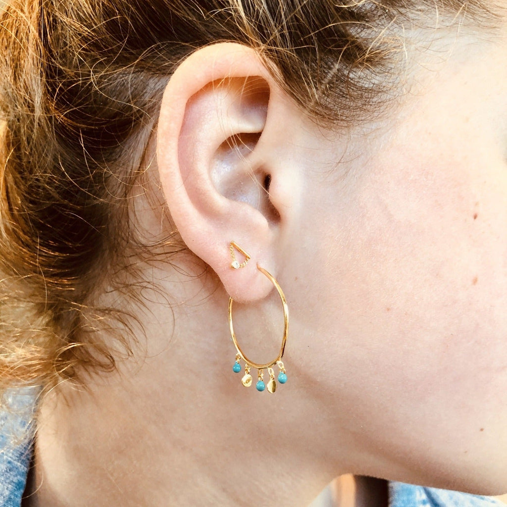 A large silver and gold plated hoop, with three turquoise beads hanging from the bottom, with two high shine gold discs in between.