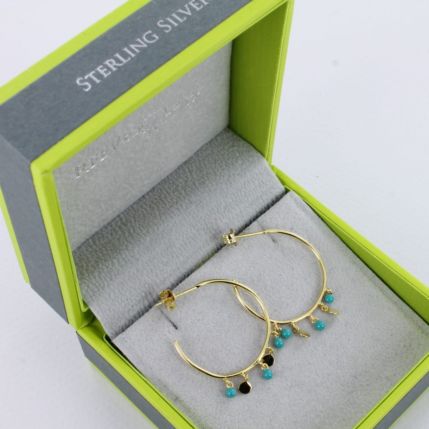 A pair of sterling silver and 18ct gold plated large hoops with three turquoise beads hanging from the bottom with two high shine gold discs in-between. Shown in a Reeves & Reeves gift box.
