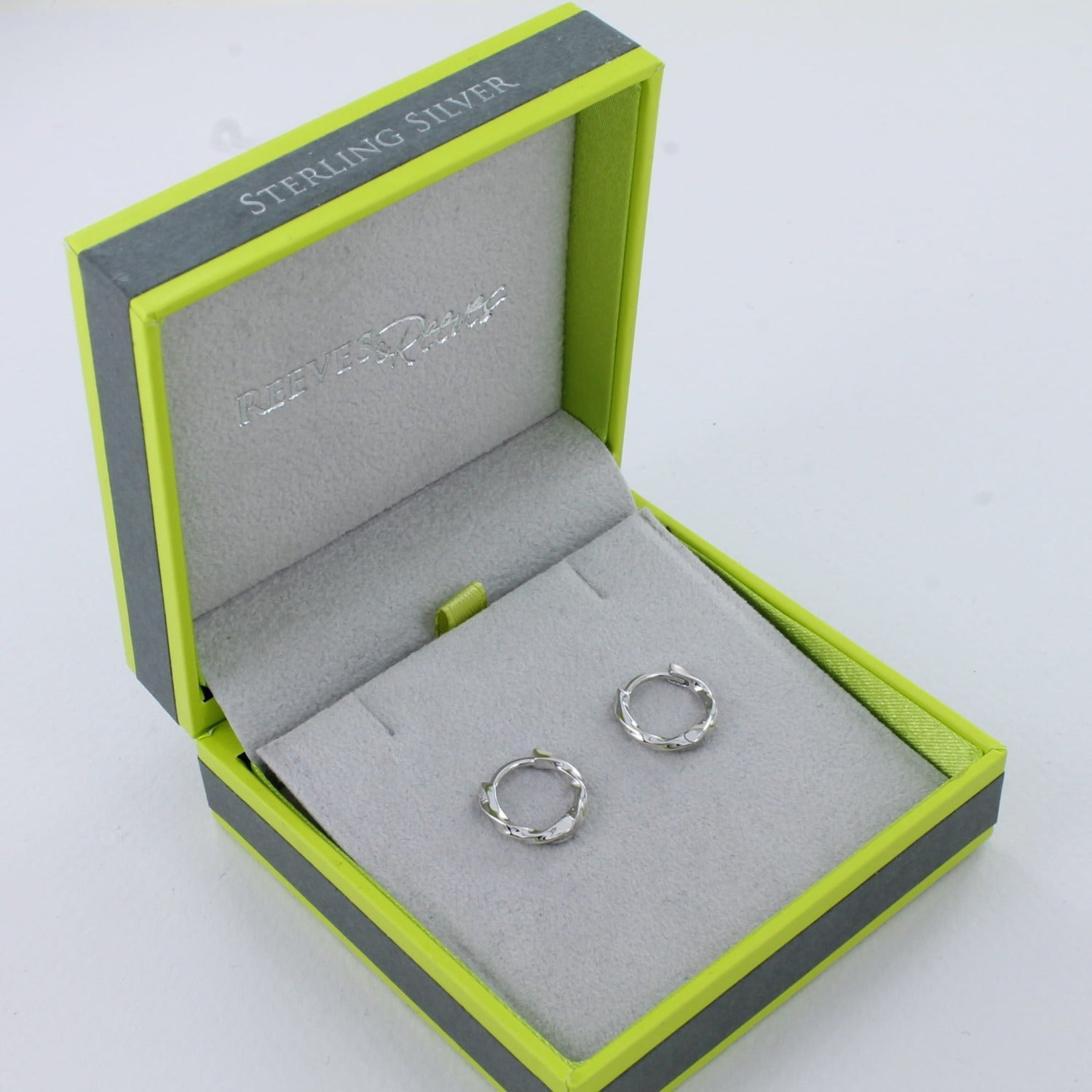 A pair of sterling silver huggie hoops in a twisted design, shown in a Reeves & Reeves gift box.