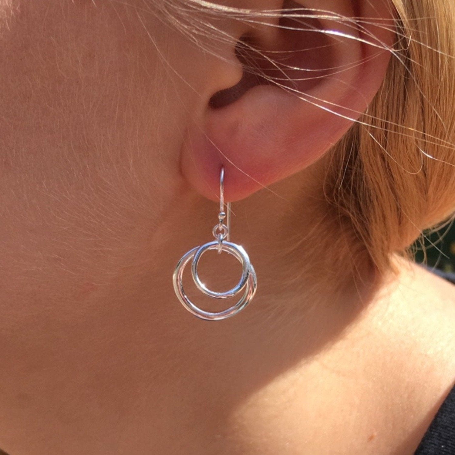 A sterling silver two ring earring, with two circle silhouettes, one smaller hanging inside the larger one, and shown in a ladies ear.