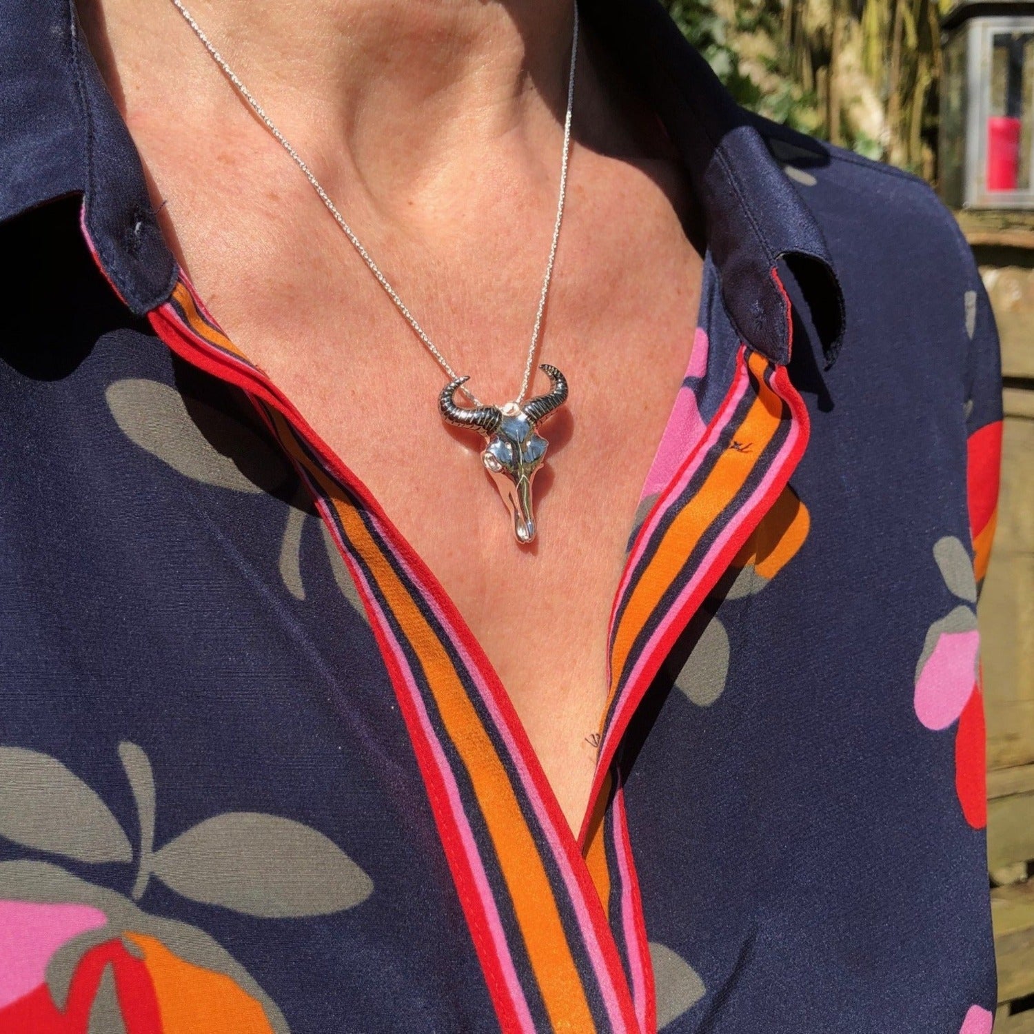 Silver Wildebeest skull pendant with black ruthenium horns, hanging on a rope style chain and worn on a model.