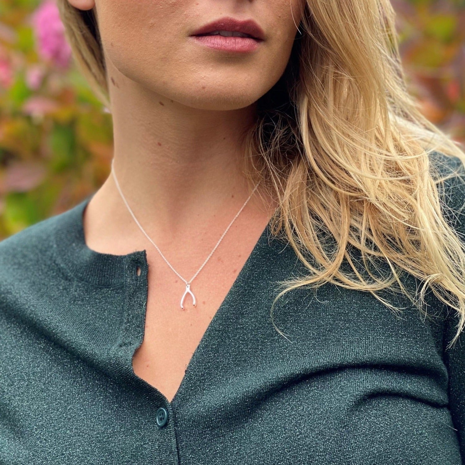 A Sterling Silver Wishbone Necklace, hanging on an adjustable silver chain, worn around a models neck.